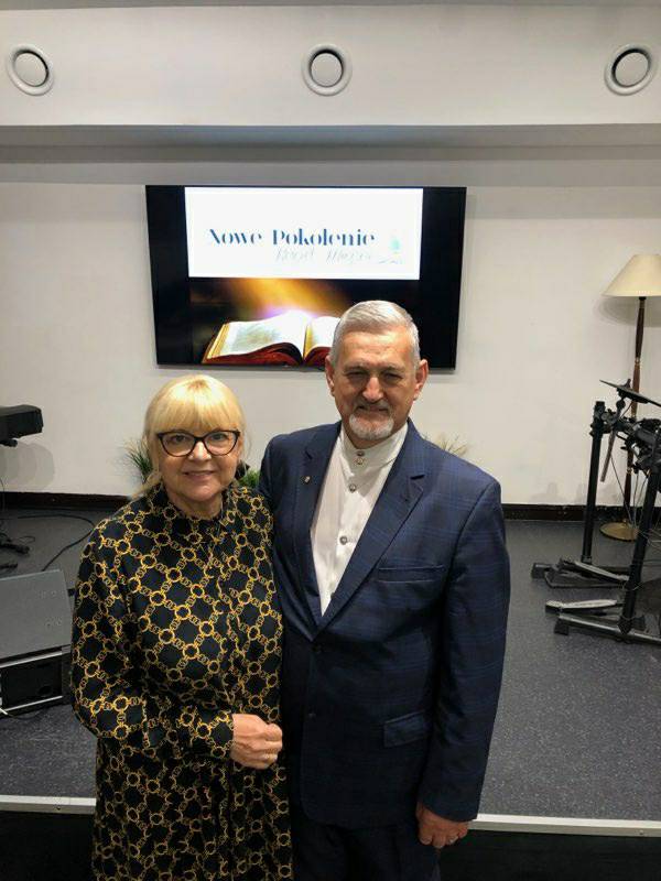 Dla Gościa 1 Pastor Aleksander Bauczyński z żoną stojący razem w sali z instrumentami muzycznymi i ekranem z napisem 'Nowe Pokolenie'. W tle otwarta księga, symbolicznie podświetlona na ekranie.
